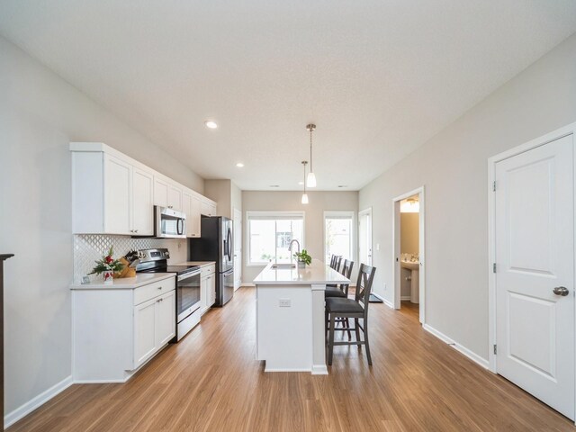 455 SW 12th St, Des Moines, IA 50309 - kitchen with decorative backsplash, stainless steel appliances, light wood-style floors, a kitchen bar, and a center island with sink