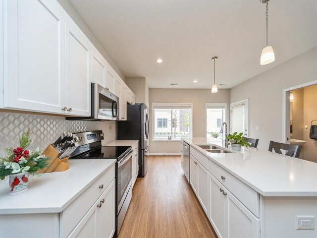 455 SW 12th St, Des Moines, IA 50309 - kitchen with a kitchen island with sink, a sink, light wood-style floors, backsplash, and appliances with stainless steel finishes
