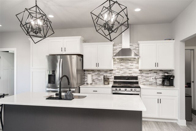 kitchen featuring stainless steel appliances, a sink, an inviting chandelier, wall chimney range hood, and light countertops