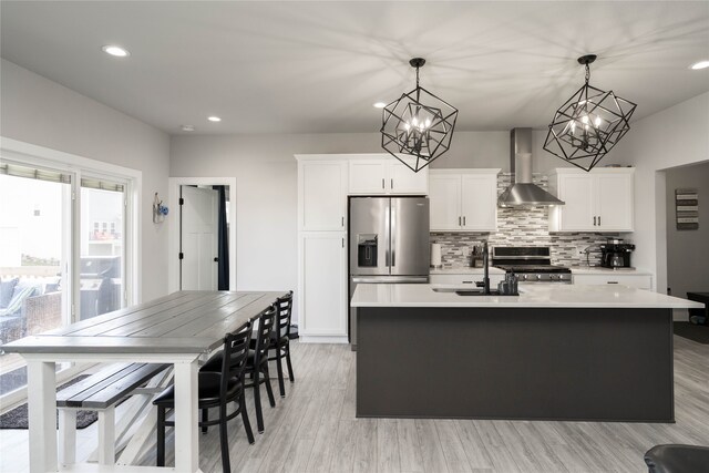 kitchen featuring a sink, an island with sink, backsplash, wall chimney exhaust hood, and appliances with stainless steel finishes