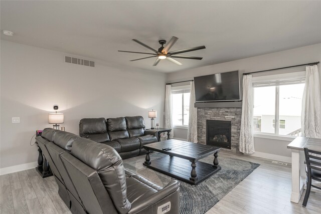 living room with ceiling fan, a stone fireplace, light wood-style floors, and visible vents