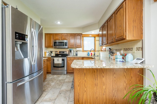 914 NE 9th St, Ankeny, IA 50021 - kitchen with a peninsula, a sink, light stone countertops, brown cabinetry, and appliances with stainless steel finishes