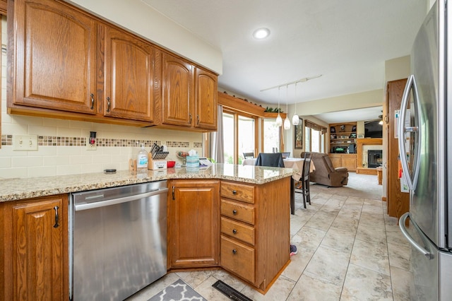 914 NE 9th St, Ankeny, IA 50021 - kitchen featuring a fireplace with raised hearth, brown cabinetry, open floor plan, stainless steel appliances, and a peninsula
