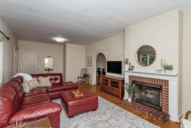 living room featuring a brick fireplace, arched walkways, and wood finished floors