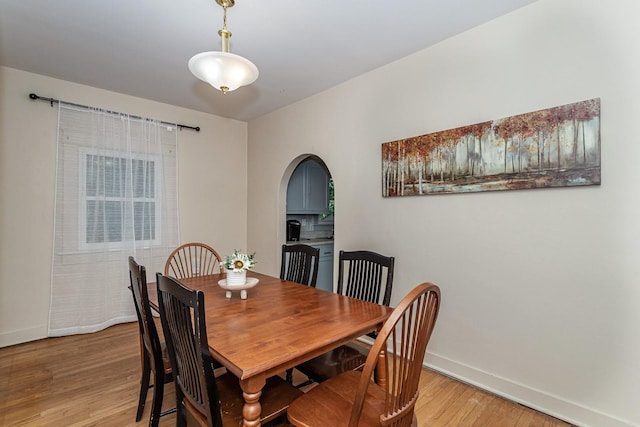 dining room with baseboards, light wood-type flooring, and arched walkways