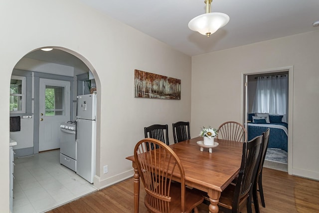 dining area with baseboards, arched walkways, and light wood-style floors