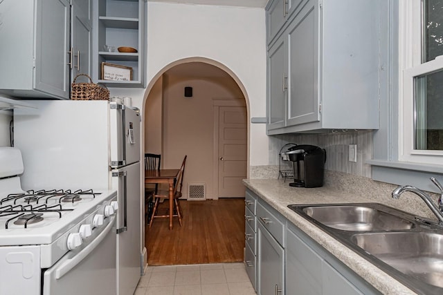 kitchen featuring visible vents, gray cabinets, white gas stove, and a sink
