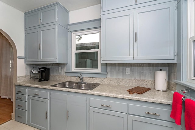 kitchen featuring gray cabinetry, arched walkways, light countertops, and a sink