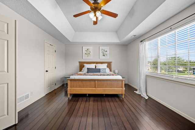 bedroom featuring visible vents, a tray ceiling, dark wood-style floors, and baseboards
