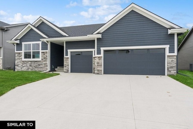 craftsman-style home with stone siding, central AC, a front yard, concrete driveway, and an attached garage