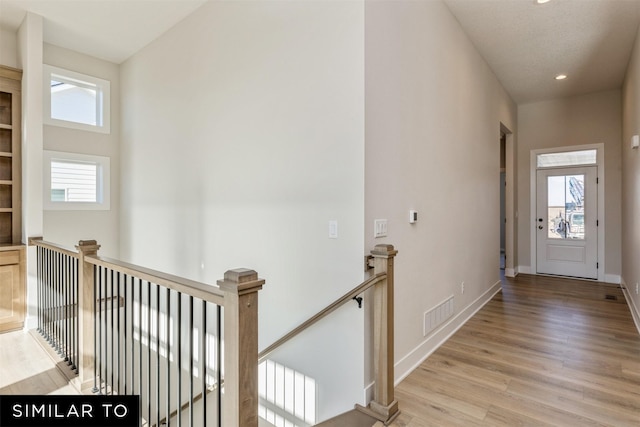 corridor featuring an upstairs landing, light wood-type flooring, and plenty of natural light