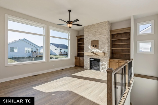 unfurnished living room featuring wood finished floors, a fireplace, baseboards, visible vents, and a ceiling fan