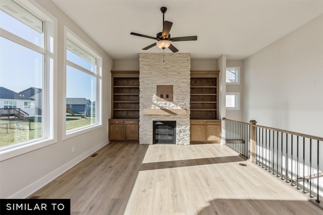 unfurnished living room with ceiling fan, visible vents, a stone fireplace, baseboards, and wood finished floors