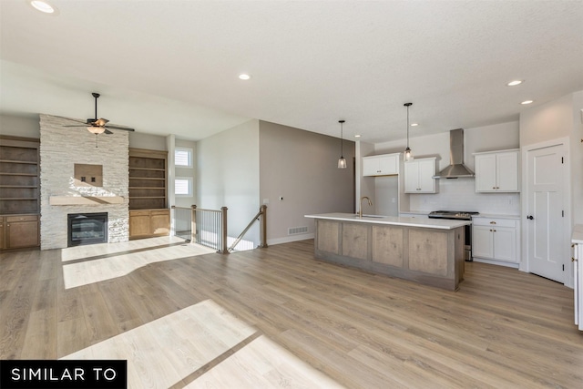 kitchen with ceiling fan, visible vents, wall chimney range hood, gas range, and open floor plan