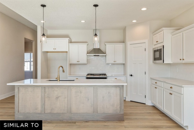 kitchen with wall chimney range hood, white cabinetry, a sink, stove, and backsplash