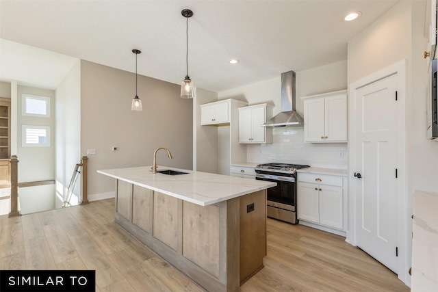 kitchen with tasteful backsplash, stainless steel gas range oven, wall chimney range hood, white cabinets, and a sink