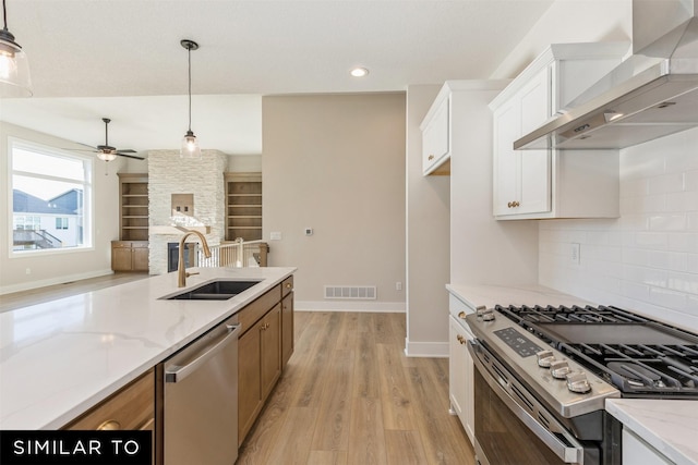 kitchen featuring stainless steel appliances, a sink, visible vents, a ceiling fan, and wall chimney exhaust hood
