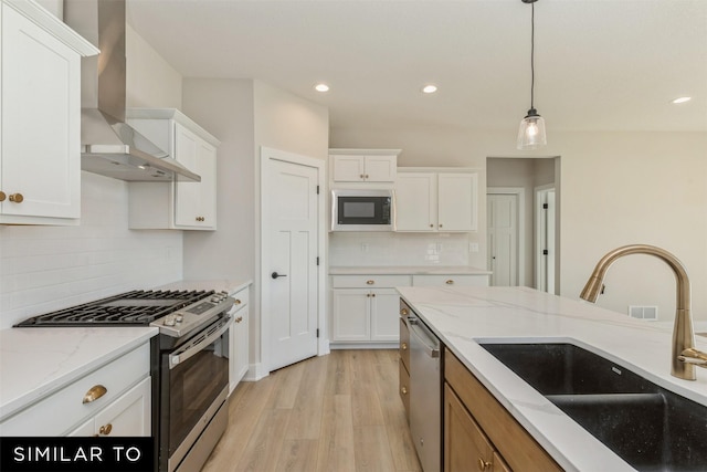 kitchen with light wood-style floors, appliances with stainless steel finishes, wall chimney range hood, white cabinets, and a sink