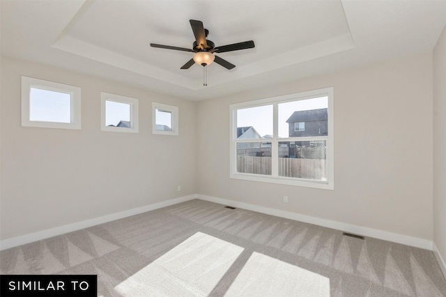 carpeted spare room with baseboards, visible vents, a ceiling fan, and a tray ceiling