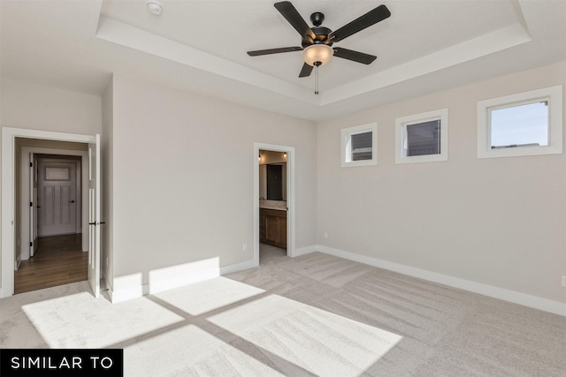 unfurnished bedroom with connected bathroom, light carpet, a tray ceiling, and baseboards