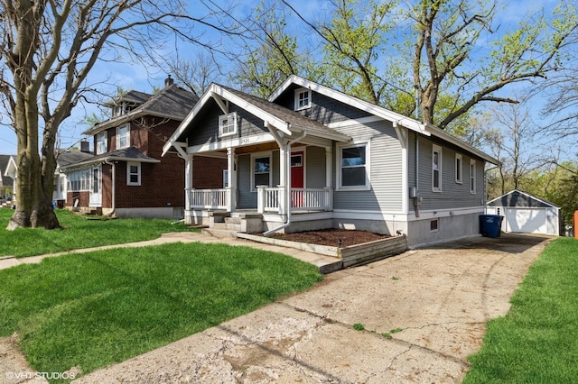 view of front facade with covered porch, an outbuilding, driveway, a detached garage, and a front lawn