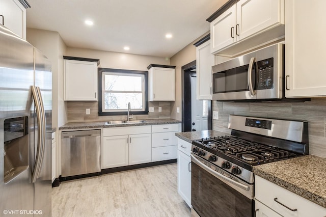 kitchen featuring dark stone countertops, tasteful backsplash, appliances with stainless steel finishes, a sink, and light wood-type flooring