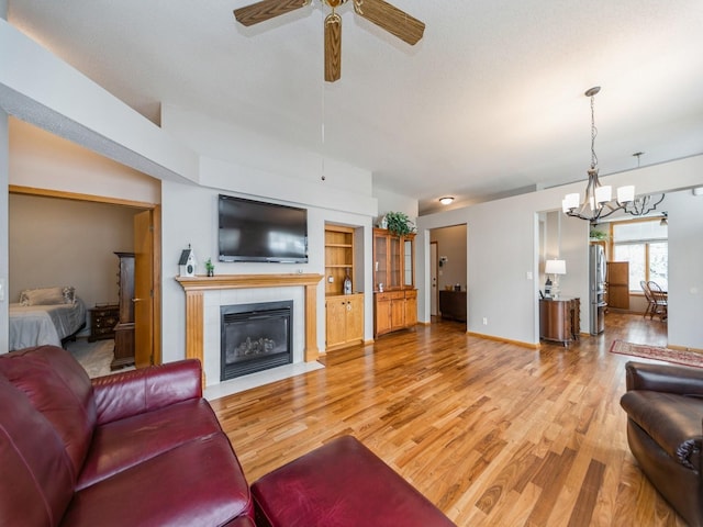 living area featuring baseboards, light wood-type flooring, ceiling fan with notable chandelier, and a fireplace with flush hearth