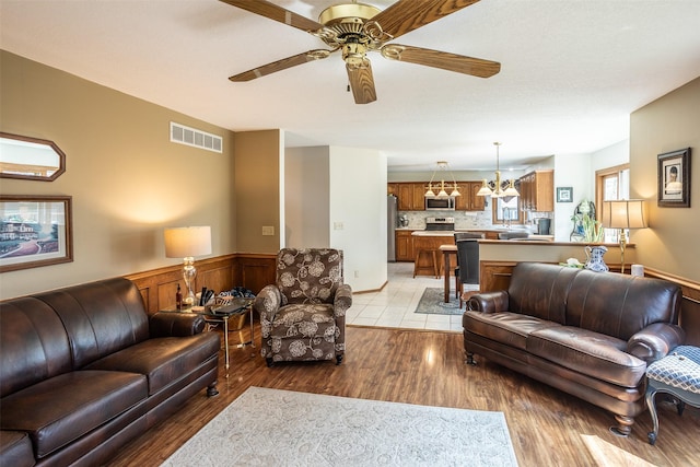 living area with visible vents, a wainscoted wall, light wood finished floors, and a ceiling fan