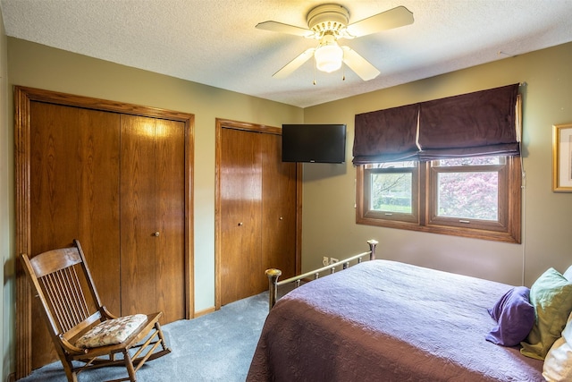 bedroom with a textured ceiling, a ceiling fan, multiple closets, and carpet floors