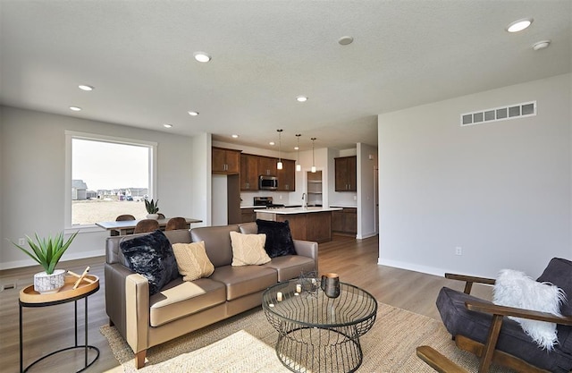 living room with baseboards, visible vents, light wood-style floors, and recessed lighting