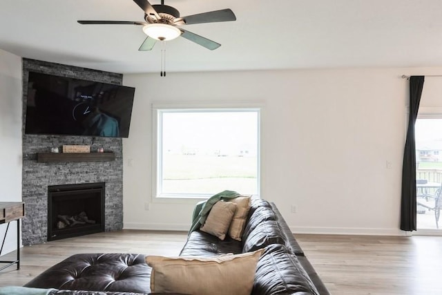 6635 NE 9th Ct, Des Moines, IA 50313 - living area with light wood-type flooring, a ceiling fan, a stone fireplace, and baseboards