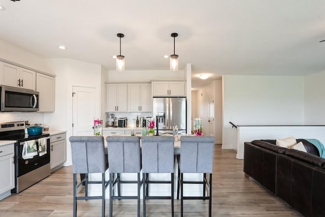 6635 NE 9th Ct, Des Moines, IA 50313 - kitchen featuring appliances with stainless steel finishes, light countertops, backsplash, light wood finished floors, and pendant lighting