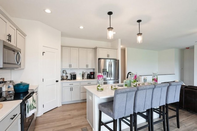 6635 NE 9th Ct, Des Moines, IA 50313 - kitchen featuring light countertops, appliances with stainless steel finishes, decorative backsplash, and light wood-type flooring