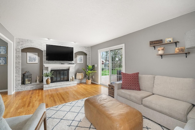 living area featuring wood finished floors, baseboards, and a brick fireplace