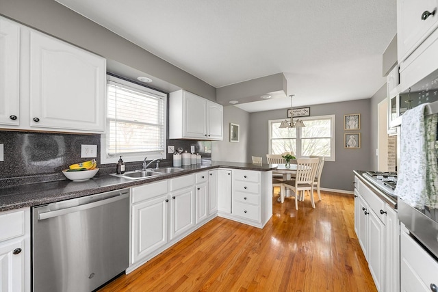 kitchen with white cabinets, a sink, appliances with stainless steel finishes, dark countertops, and light wood-style floors