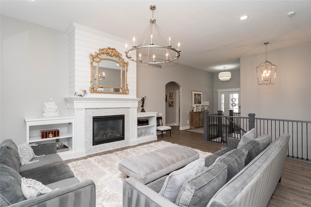 living area featuring arched walkways, an inviting chandelier, a glass covered fireplace, recessed lighting, and wood finished floors
