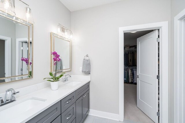 bathroom with a walk in closet, double vanity, a sink, and baseboards
