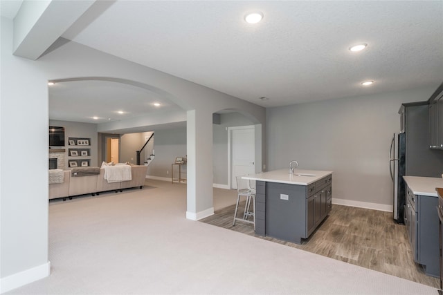 kitchen with arched walkways, an island with sink, a sink, gray cabinetry, and a kitchen breakfast bar