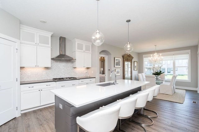 kitchen featuring wall chimney exhaust hood, arched walkways, wood finished floors, a sink, and gas cooktop