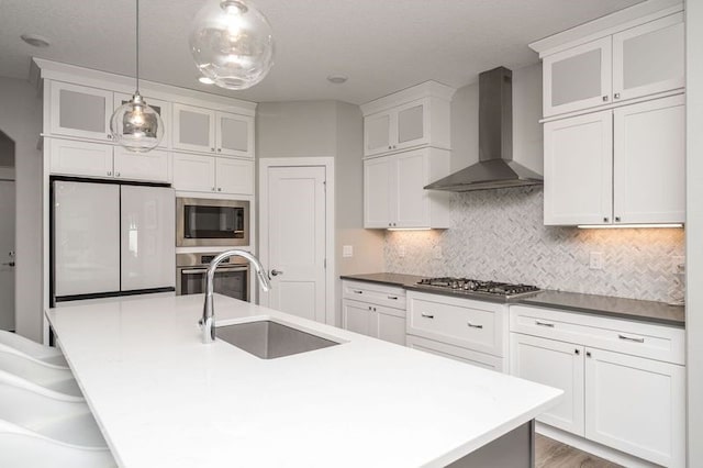 kitchen with white cabinets, stainless steel appliances, wall chimney exhaust hood, and a sink