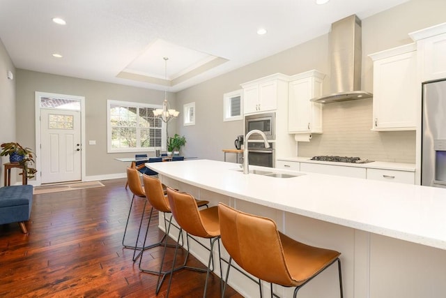 1616 Park Ave, Des Moines, IA 50315 - kitchen featuring wall chimney exhaust hood, a chandelier, backsplash, dark wood finished floors, and white cabinetry