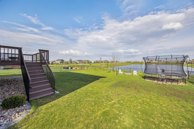 view of yard with fence, stairway, a water view, and a trampoline