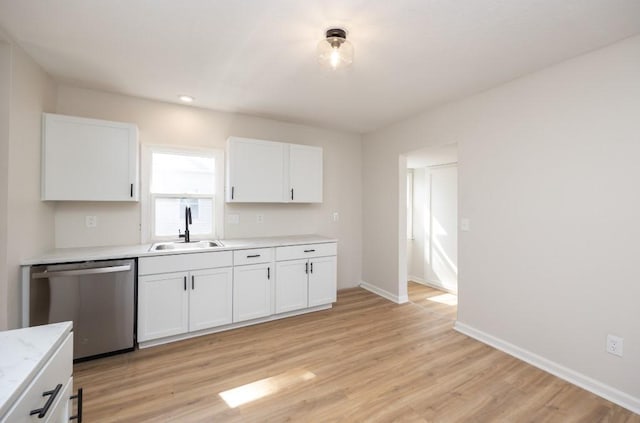 kitchen with stainless steel dishwasher, light wood-style flooring, white cabinets, a sink, and baseboards