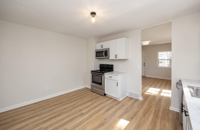 kitchen with light wood-style flooring, stainless steel appliances, white cabinets, baseboards, and visible vents