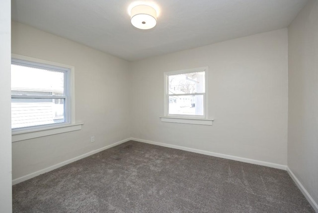empty room with dark colored carpet, a wealth of natural light, and baseboards