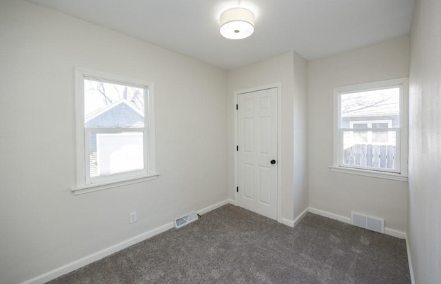 empty room featuring dark colored carpet, a wealth of natural light, and visible vents