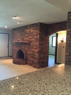 1301 Florida Ave, Ames, IA 50014 - unfurnished living room with speckled floor, a brick fireplace, a baseboard heating unit, brick wall, and arched walkways