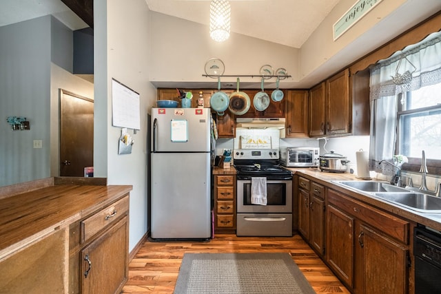 kitchen with stainless steel appliances, under cabinet range hood, vaulted ceiling, a sink, and light wood-type flooring