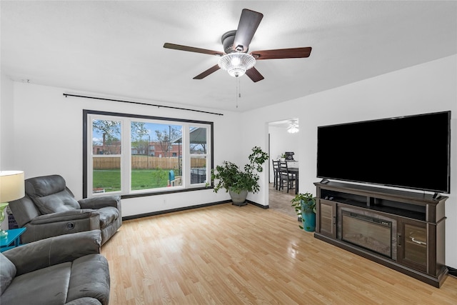 living area featuring light wood-style floors, a ceiling fan, and baseboards