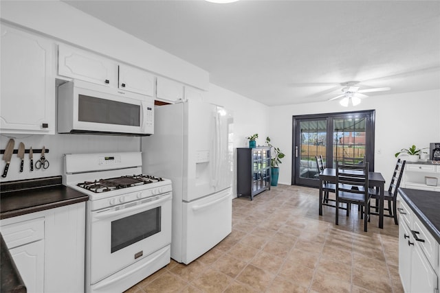 kitchen featuring white cabinetry, dark countertops, a ceiling fan, and white appliances